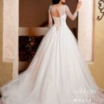 Bride in a long white wedding gown, standing gracefully at the entrance of a beautiful building and striking a pose with her back to the camera